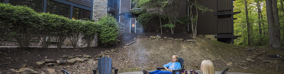 Two people sitting in Adirondack chairs around a fire pit.